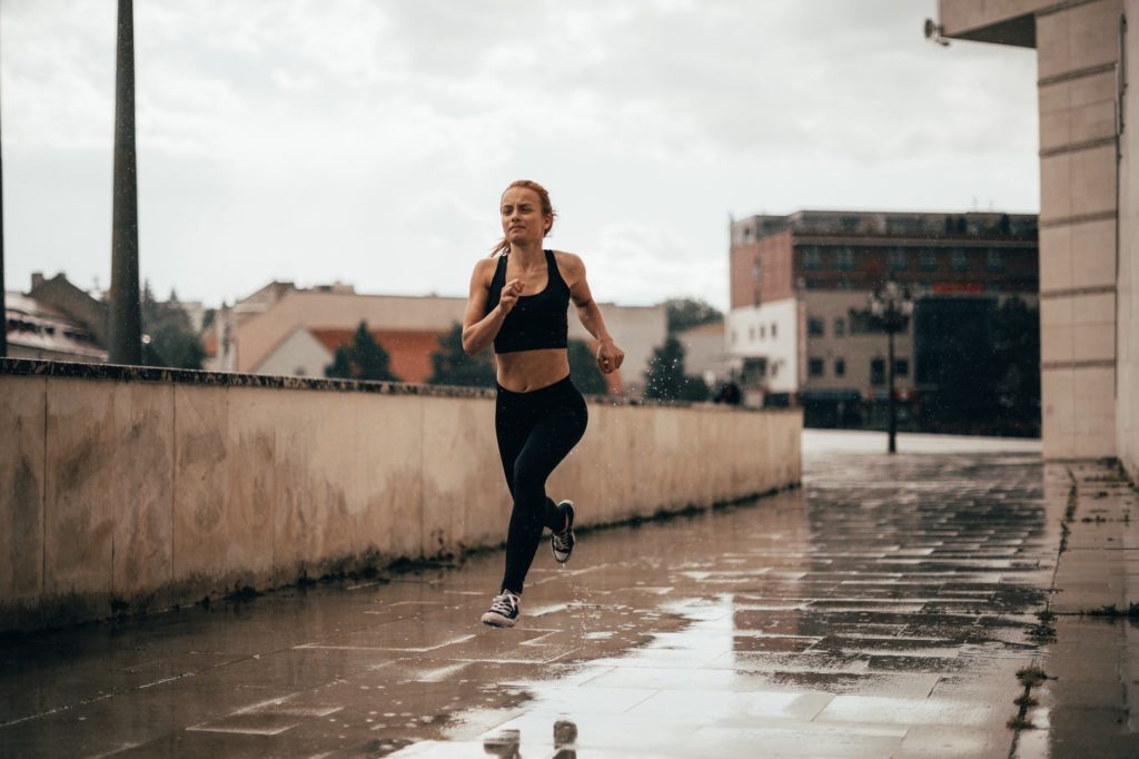 active young woman running along street near buildings on rainy day