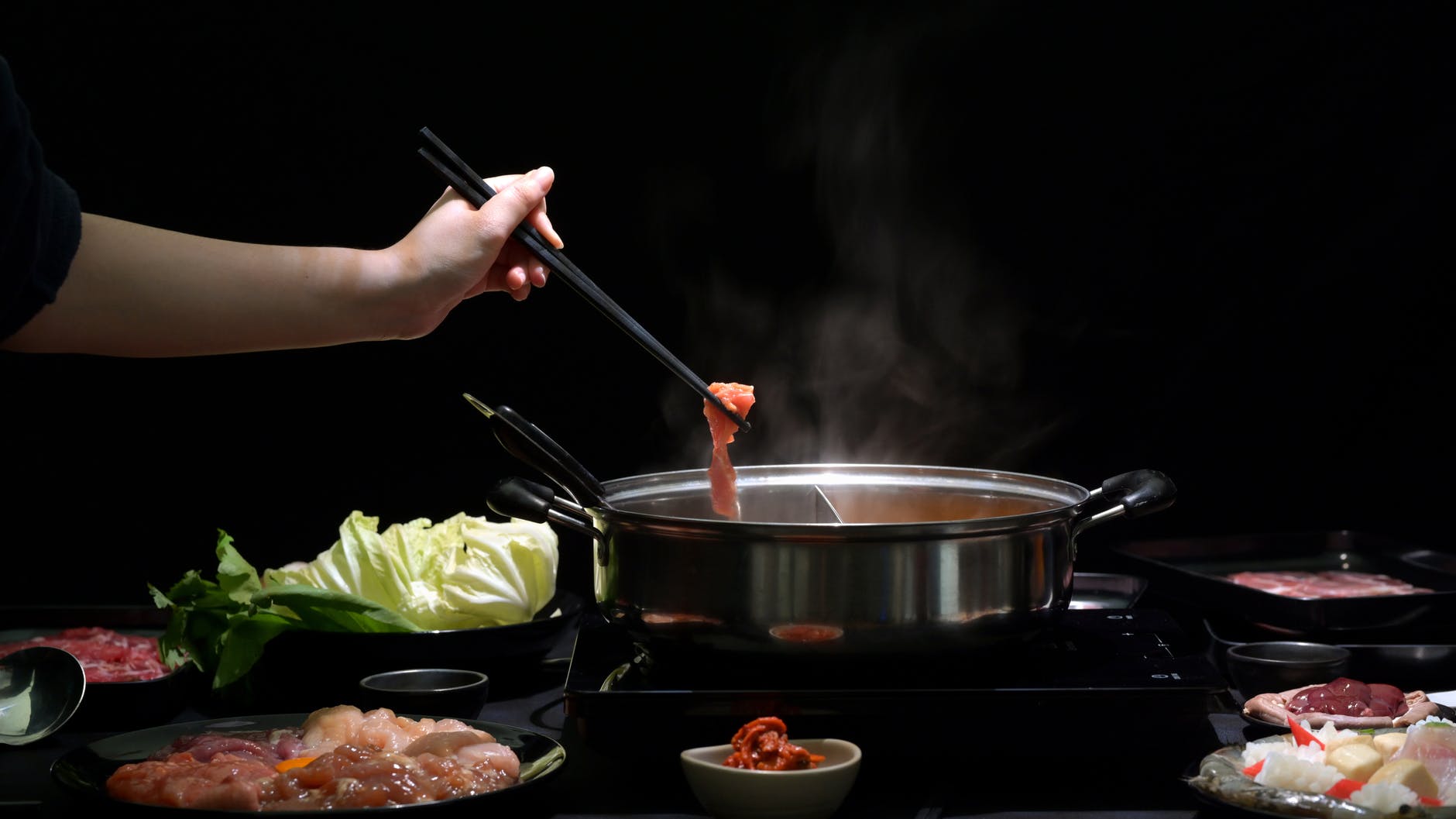 person holding black chopsticks and green vegetable on stainless steel cooking pot