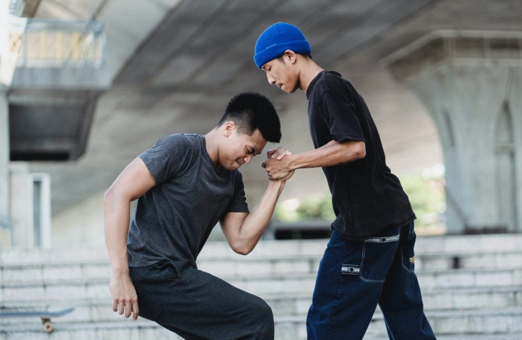 young man helping friend to stand up in skate park