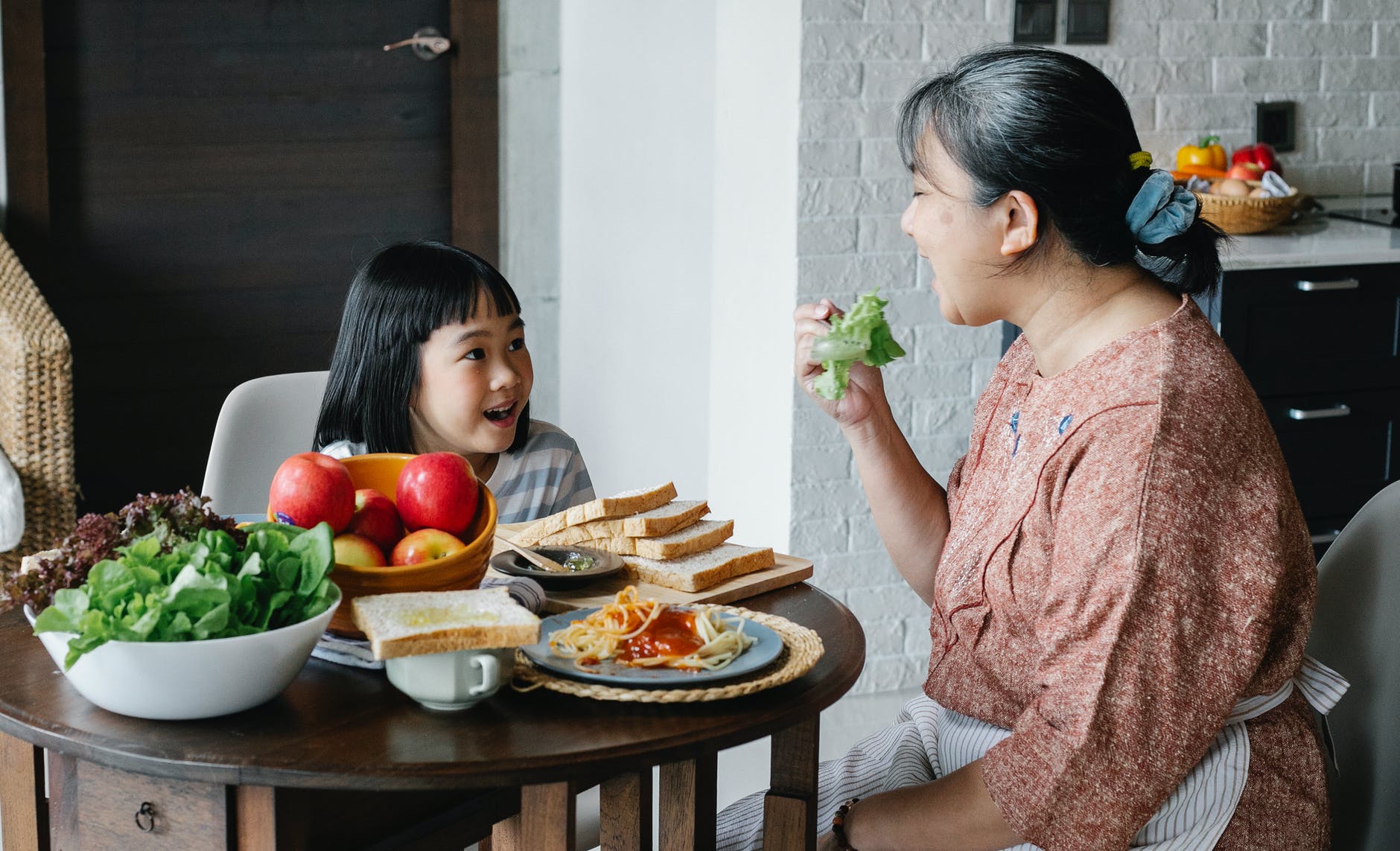 delighted ethnic little girl looking at grandmother eating healthy salad