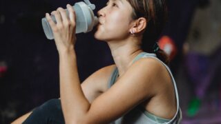 thirsty ethnic sportswoman drinking water after bouldering workout