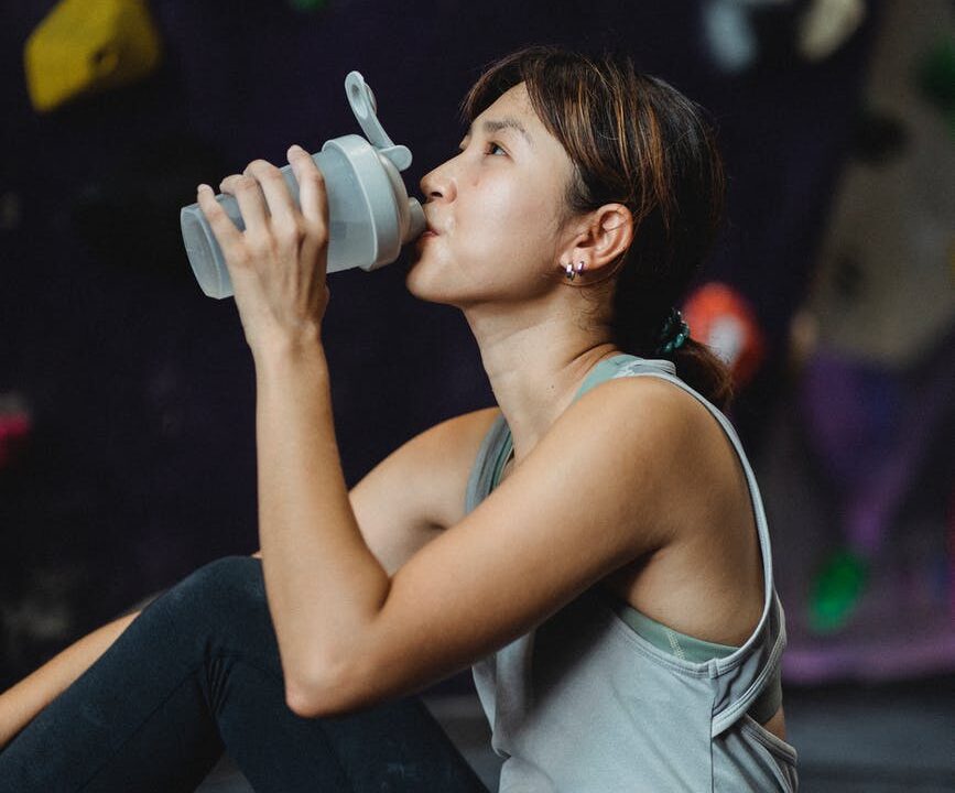 thirsty ethnic sportswoman drinking water after bouldering workout