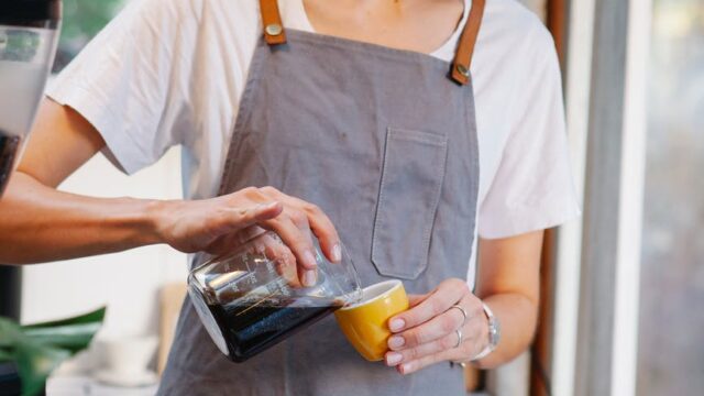 woman pouring fresh aromatic coffee from jug into cup