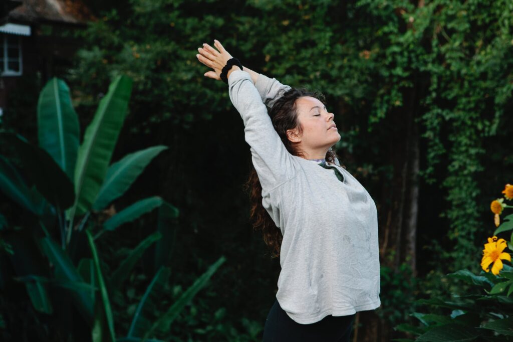 woman with eyes closed stretching among green tropical trees