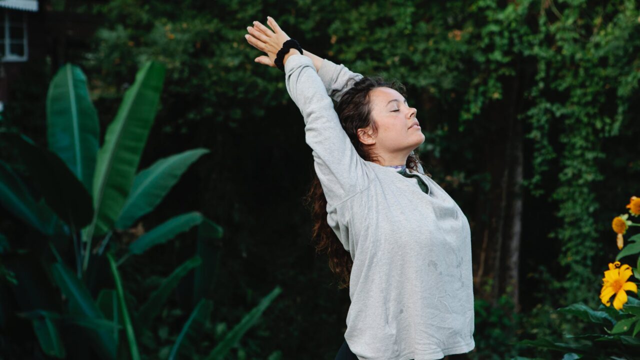 woman with eyes closed stretching among green tropical trees