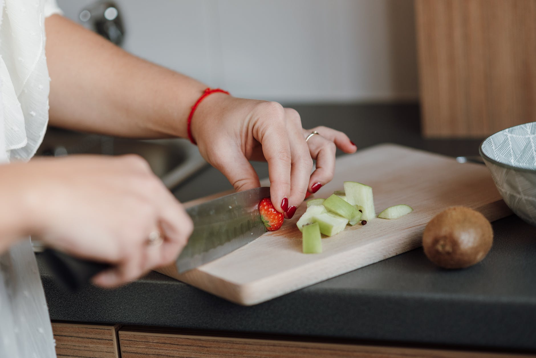 crop woman cutting strawberry near sliced apple in kitchen