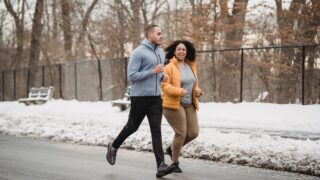 ethnic trainer and woman jogging on snowy street