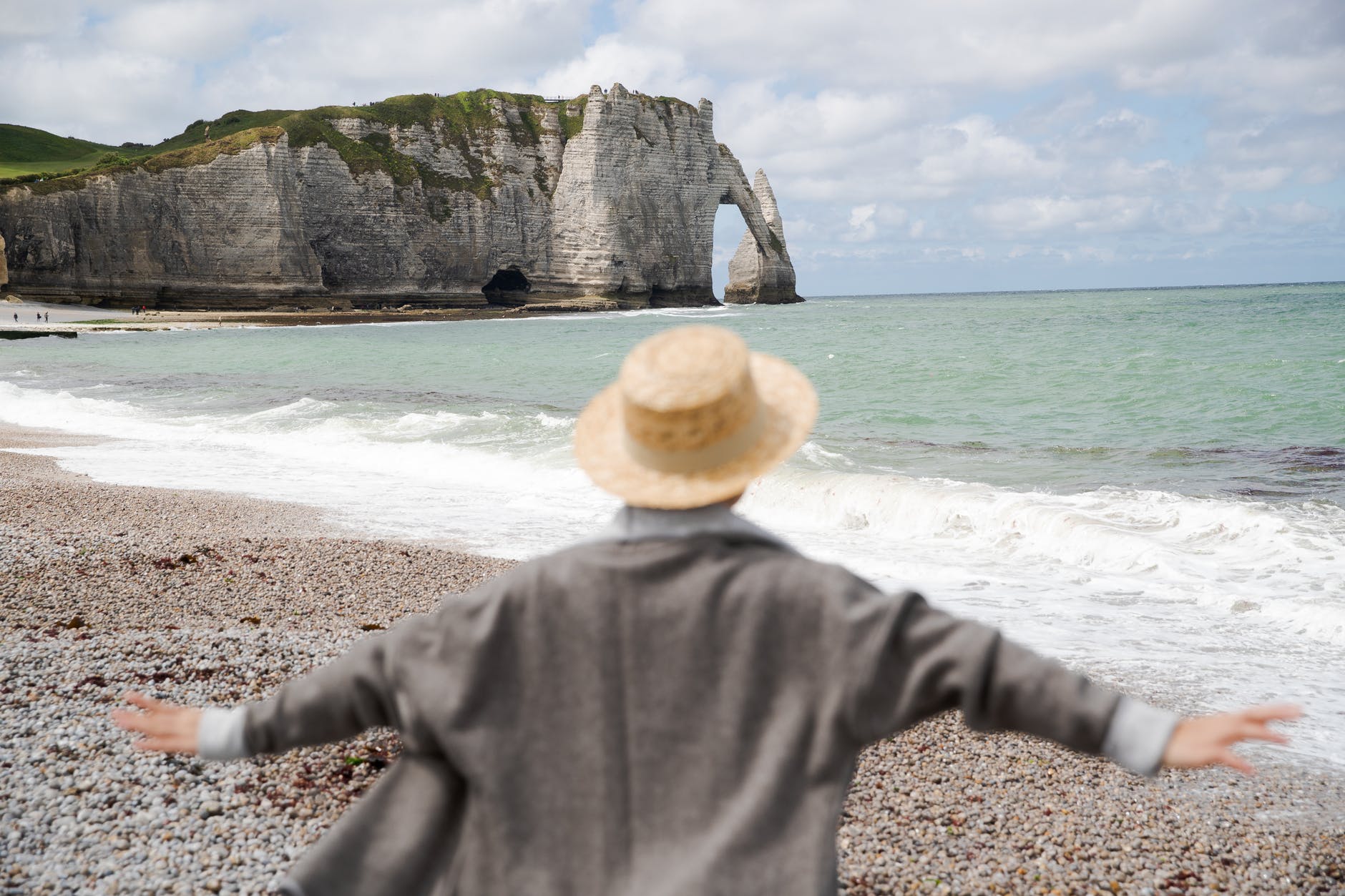 unrecognizable traveler in hat on shore near wavy sea