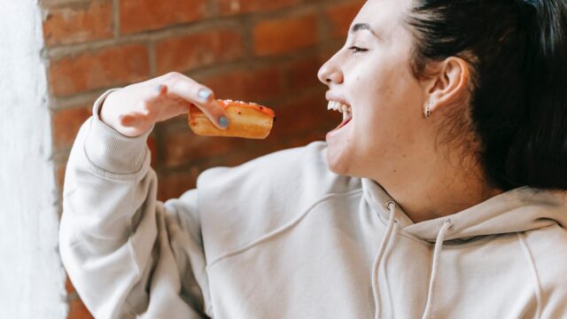 crop excited woman eating fresh yummy donut